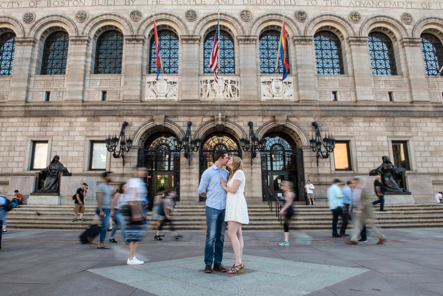 boston engagement photo where couple stands together in front of Boston Public Library and a crowd seems to rush around them. they are still and everyone else is in motion blur